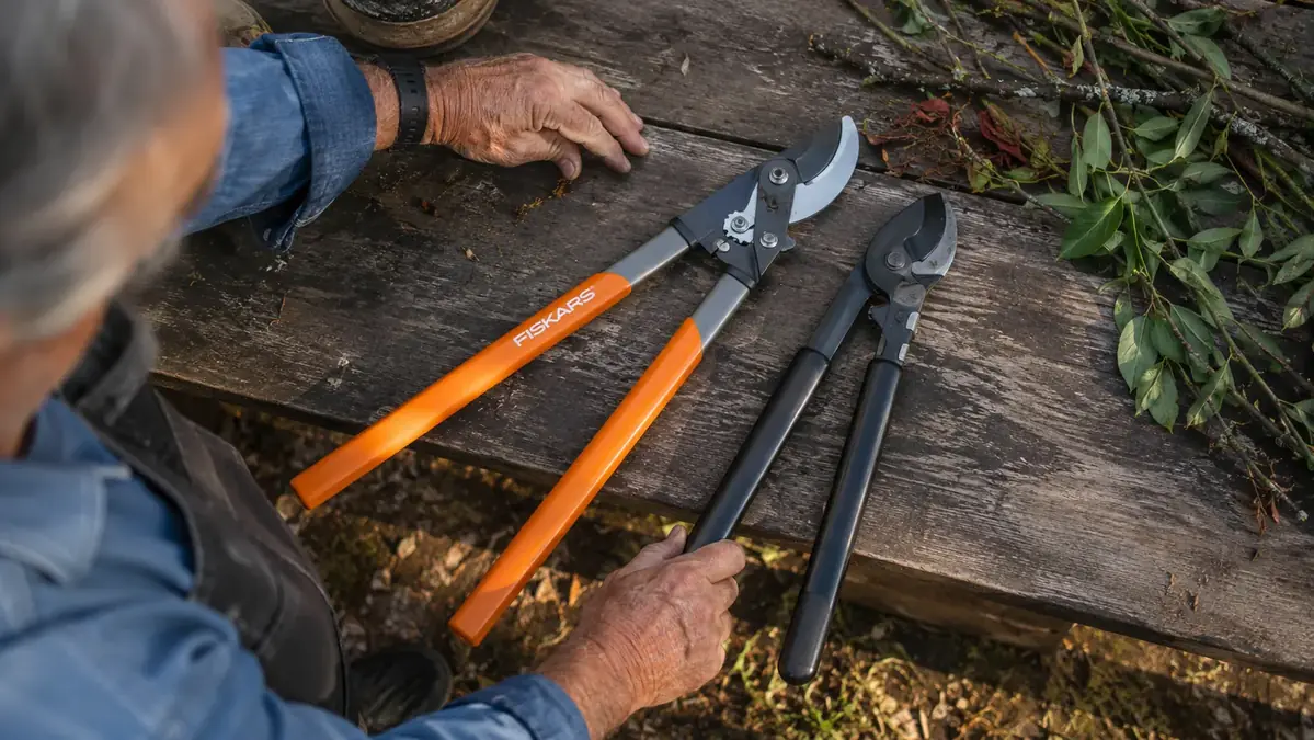 Fiskars 28 inch bypass loppers and a generic anvil lopper laid side by side on a wooden potting bench with cut branches
